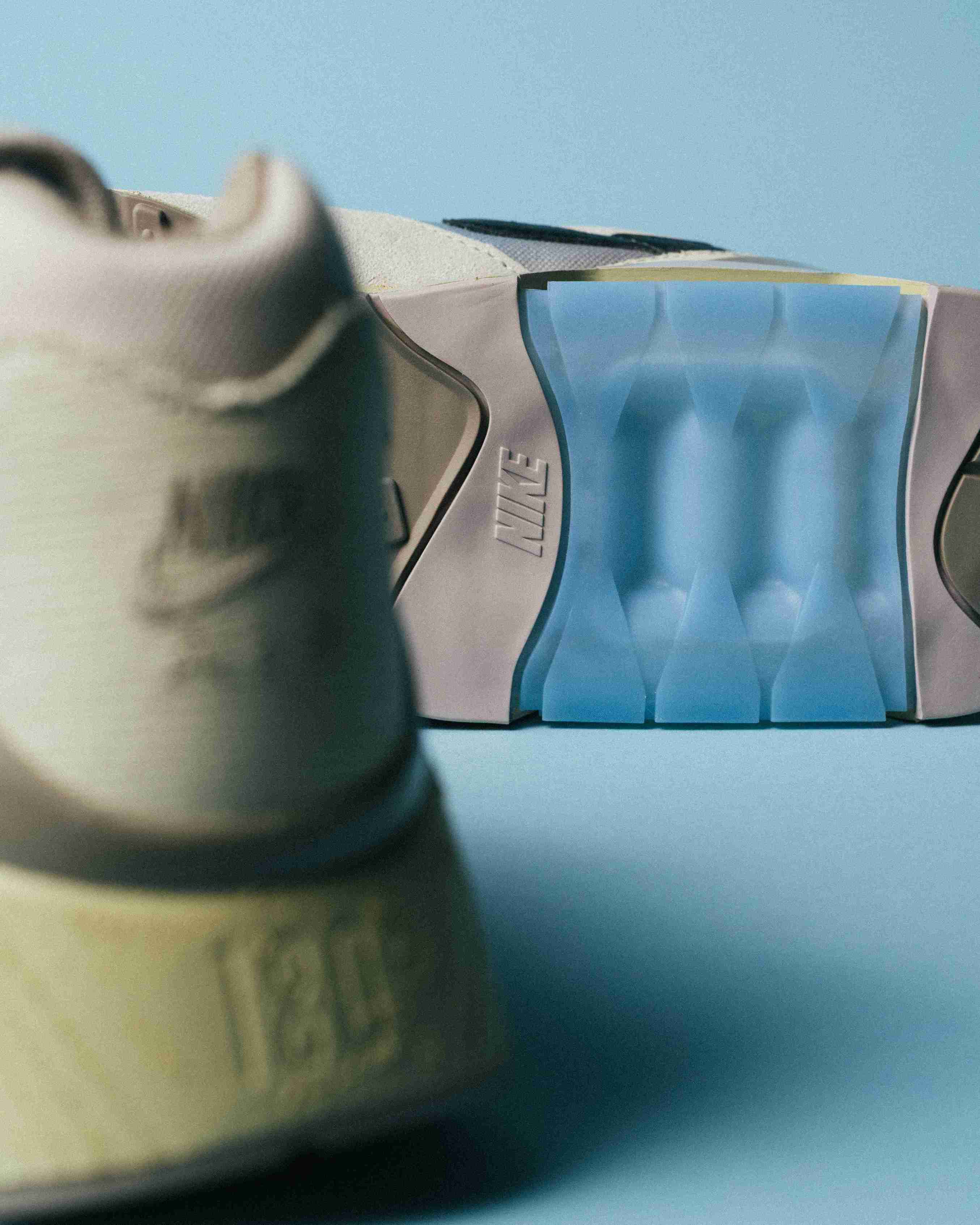 Paire de sneakers beige et bleu clair posée sur un fond bleu, vue de trois quarts avec mise en avant des formes et détails du modèle.